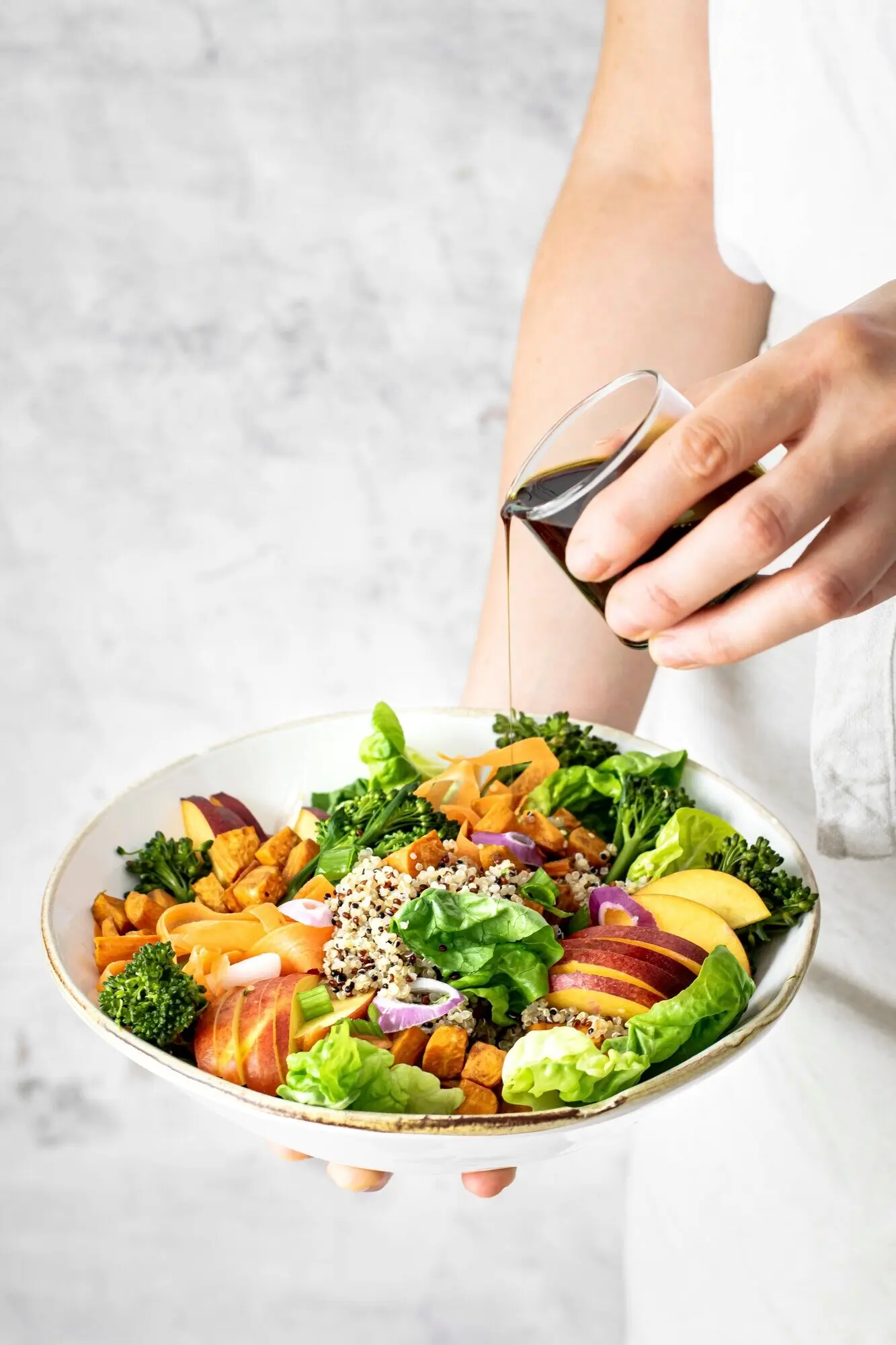 Eine Frau übergießt eine Süßkartoffel-Buddha-Bowl mit Kürbiskernöl.
